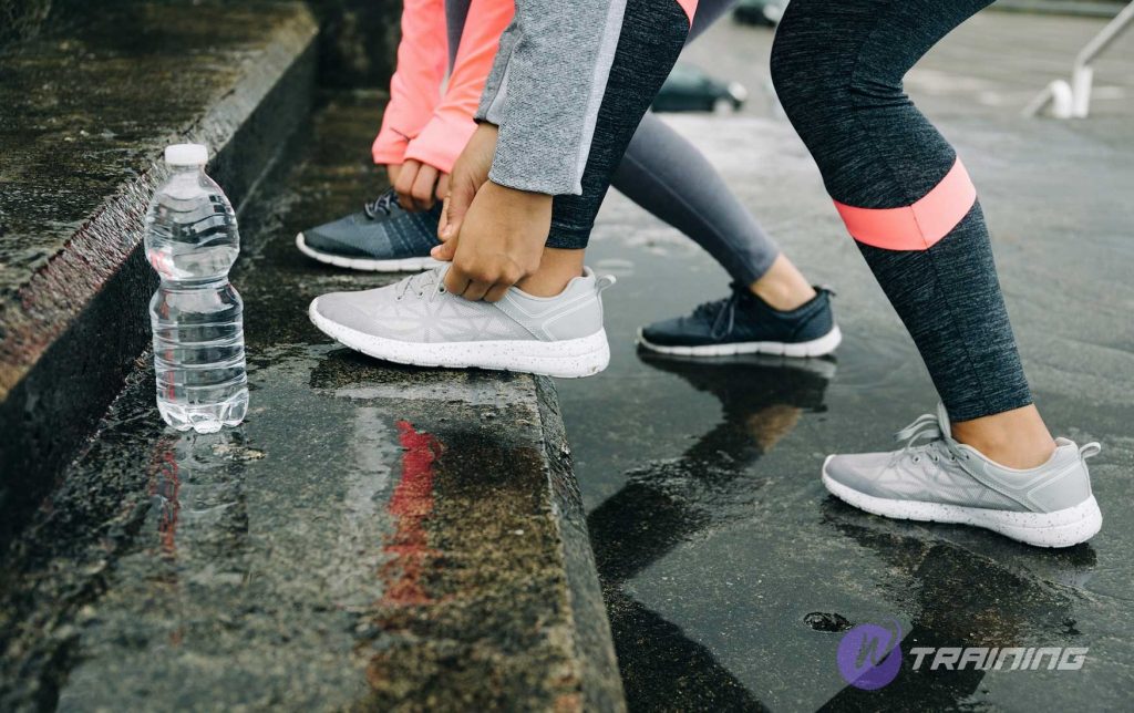 two girls tight their shoelaces to run in rain