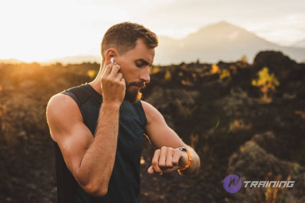 Male runner synchronizing true wireless earbuds with smart watch. Preparing for trail running outdoors at sunrise.