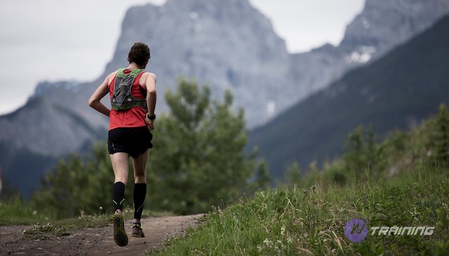 A man competes in a long distance cross country trail running race in the Rocky Mountains of Canada. He wears compression socks and a hydration back pack.